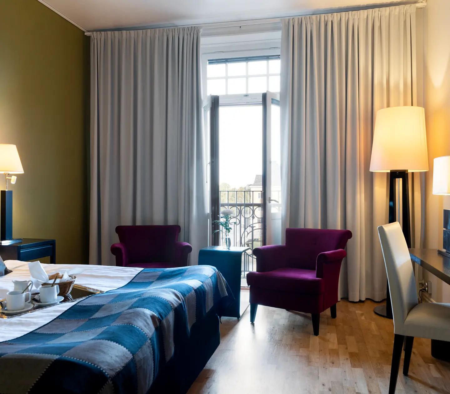 Bright hotel room with bed, desk and purple armchairs