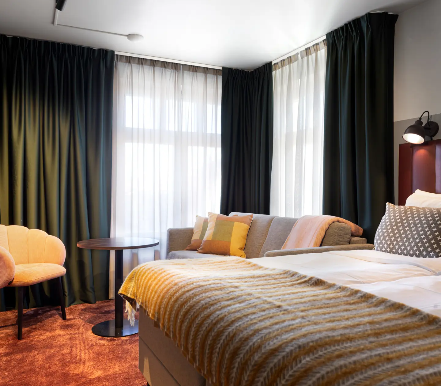 Comfortable hotel room with double bed, sofa group and curtains