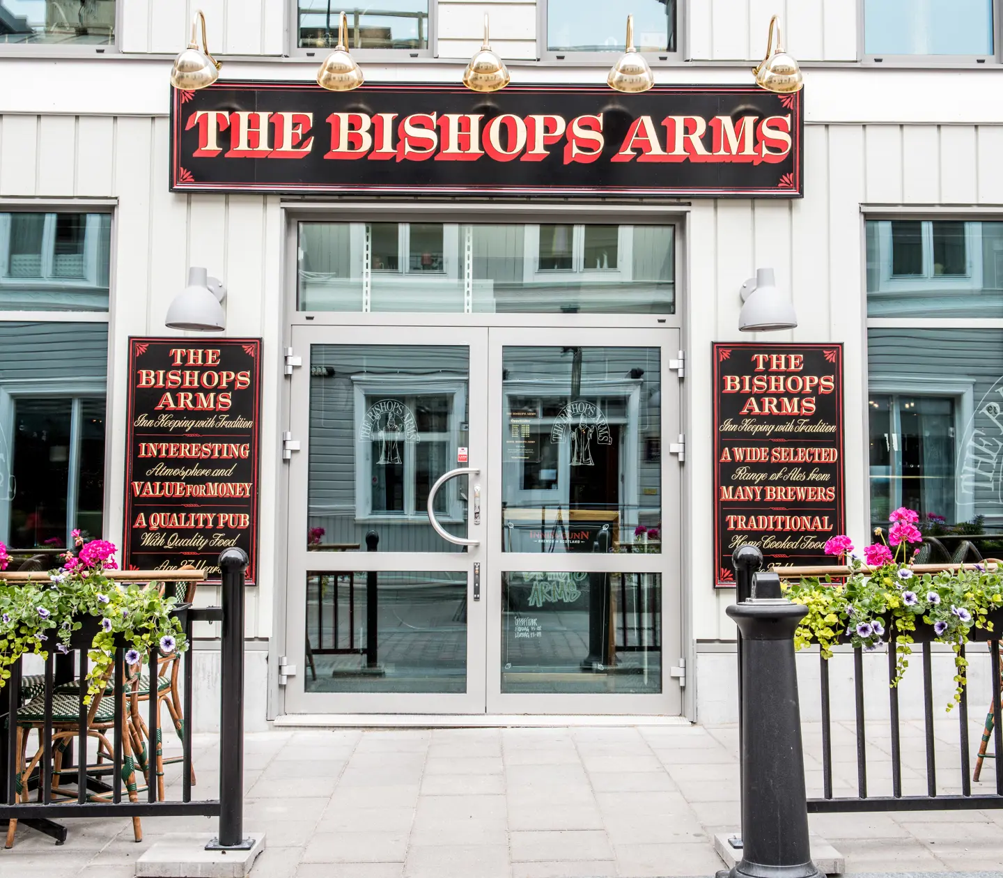 Entrance to The Bishops Arms with large glass doors, flowers and signs