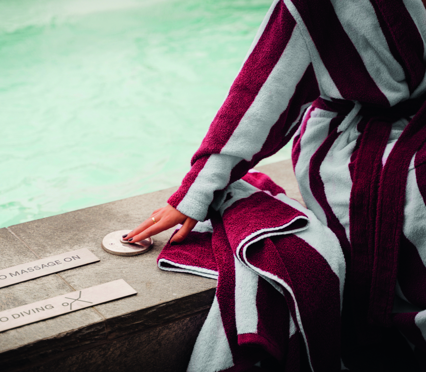 A woman in a bathrobe sitting by a pool