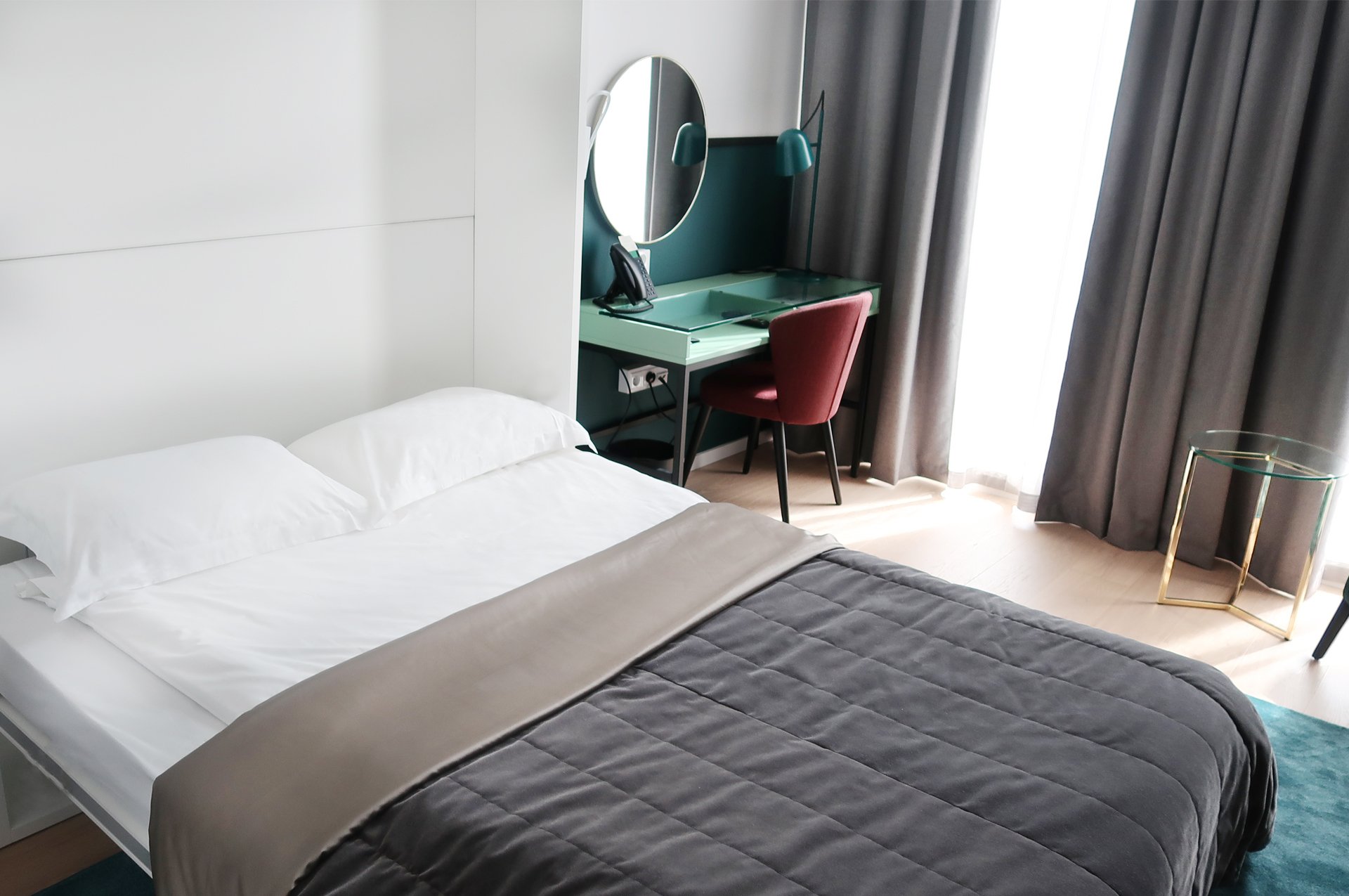Ljust hotellrum med säng, skrivbord och spegel
