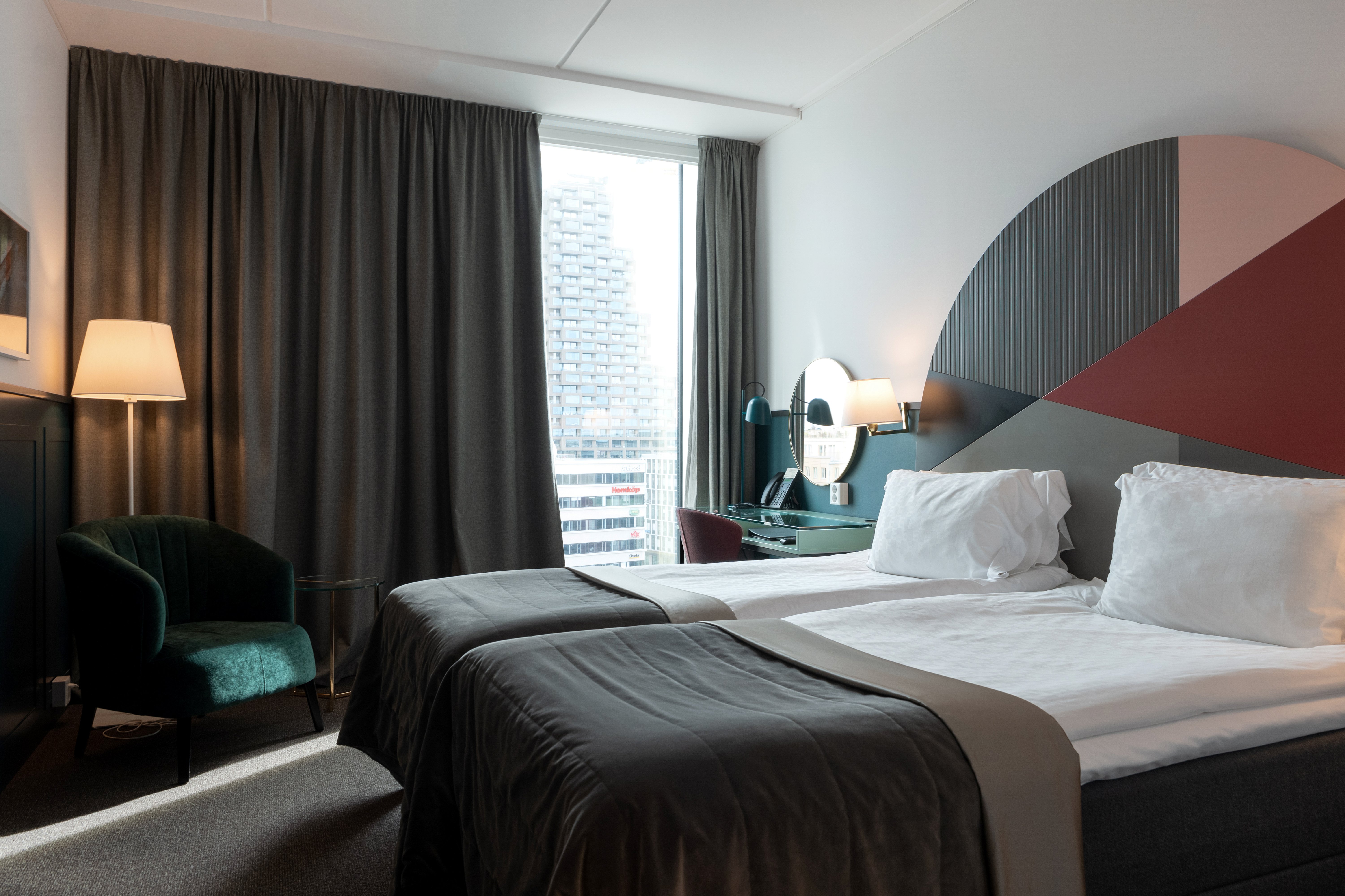 Ljust hotellrum med sängar, färgglad sänggavel och fönster