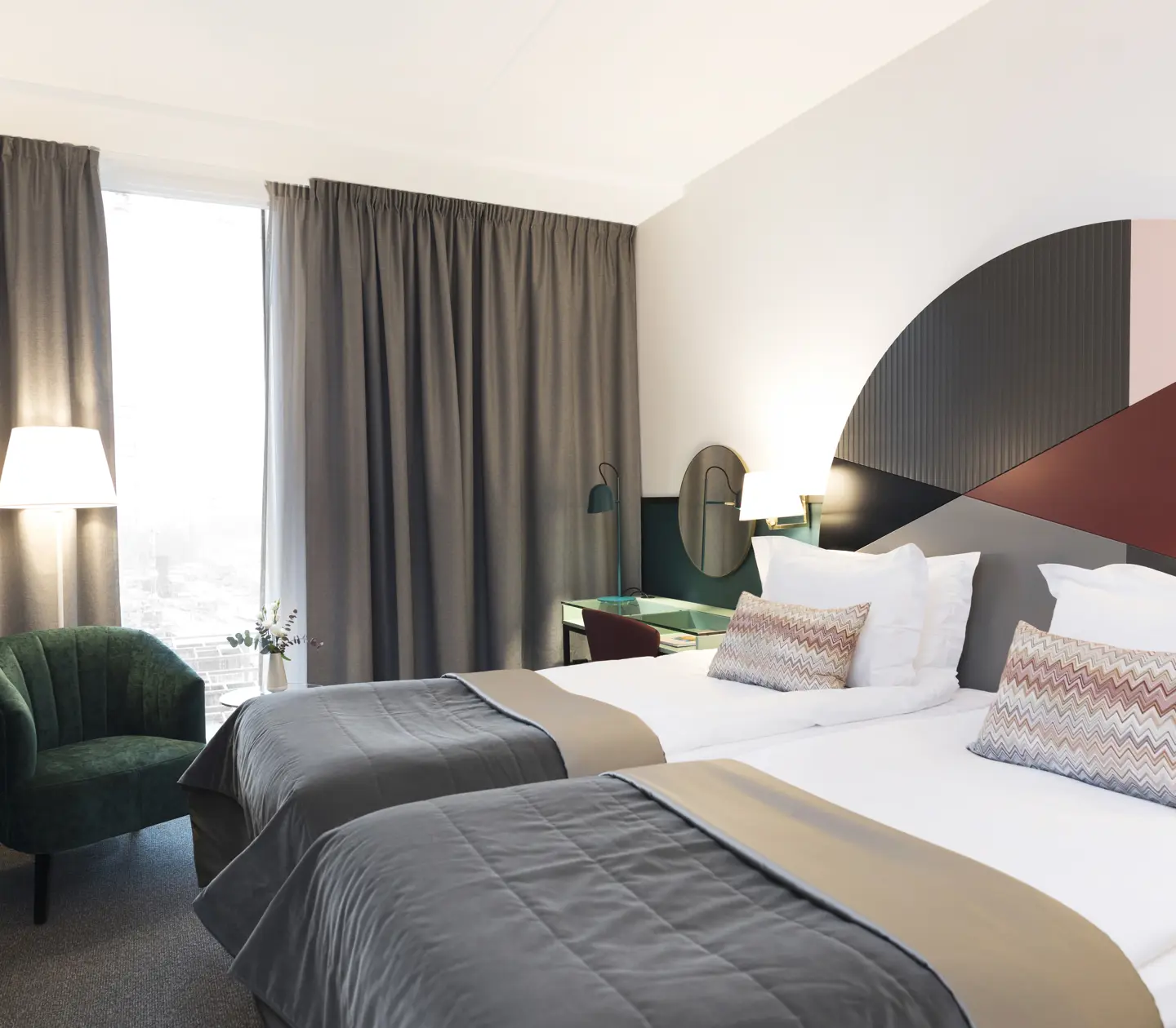 Bright hotel room with beds, colorful headboard and green armchair