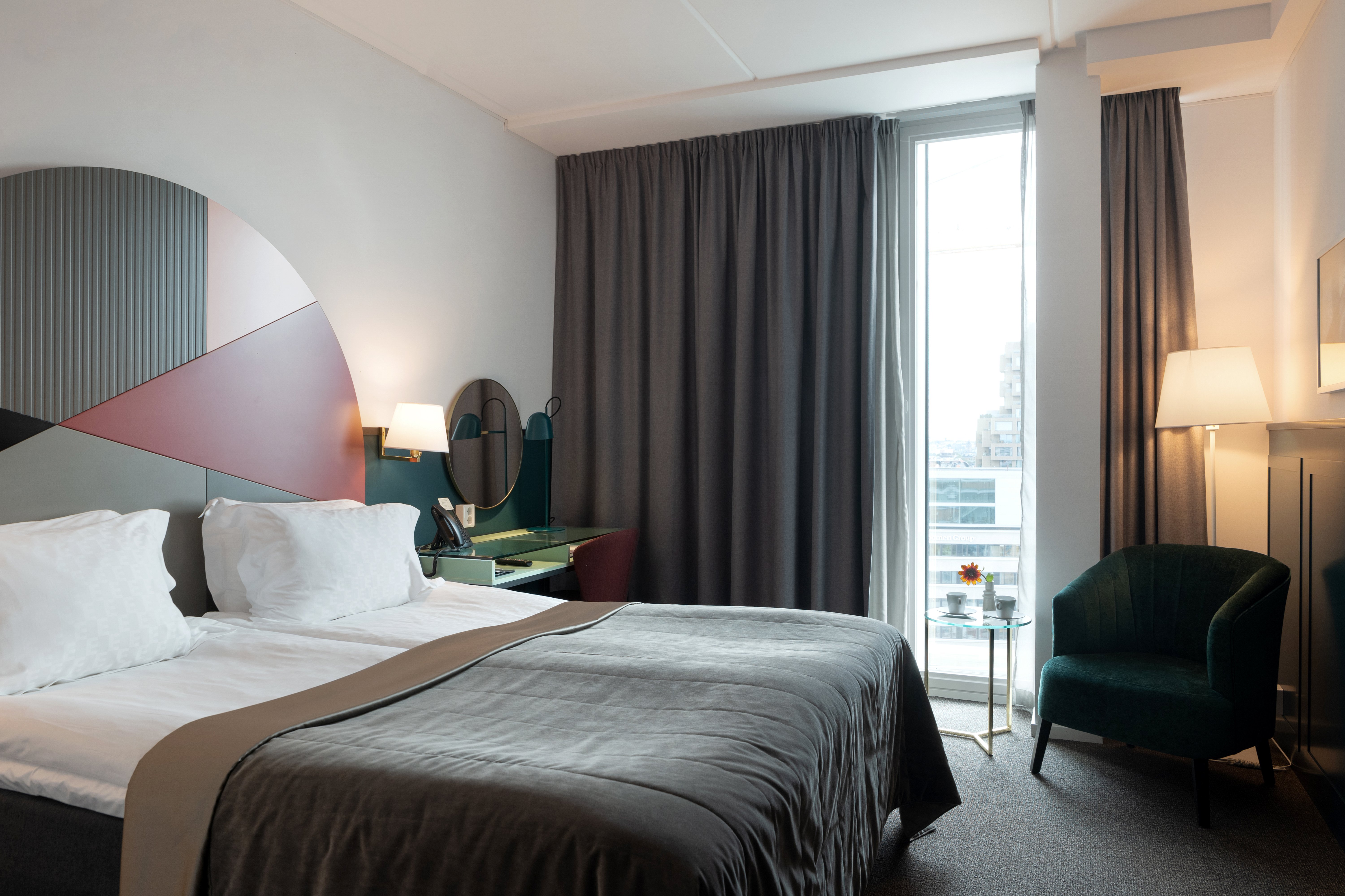 Ljust hotellrum med säng, färgglad sänggavel och fönster