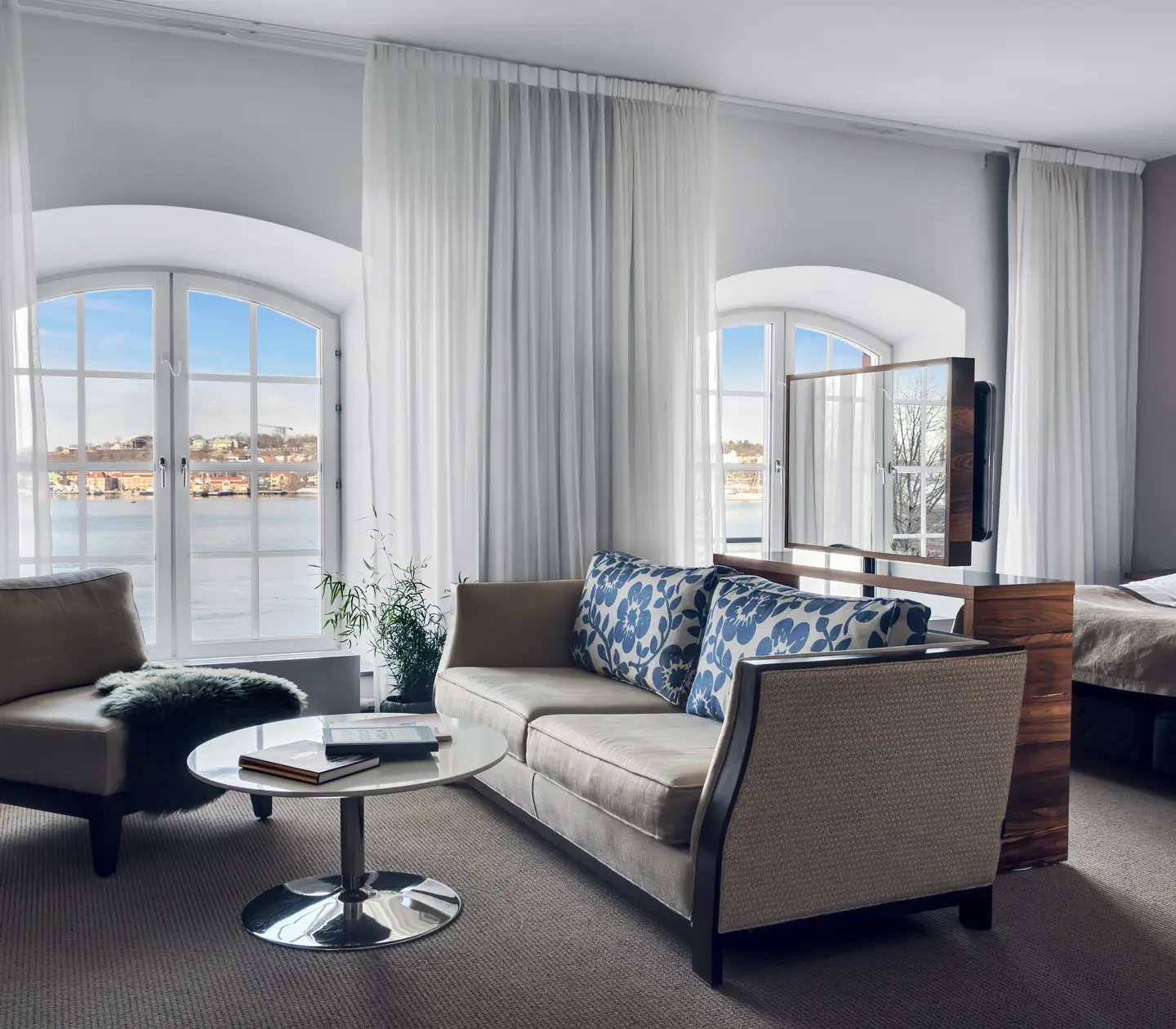 Bright hotel room with bed, sofa group and large windows with sea view
