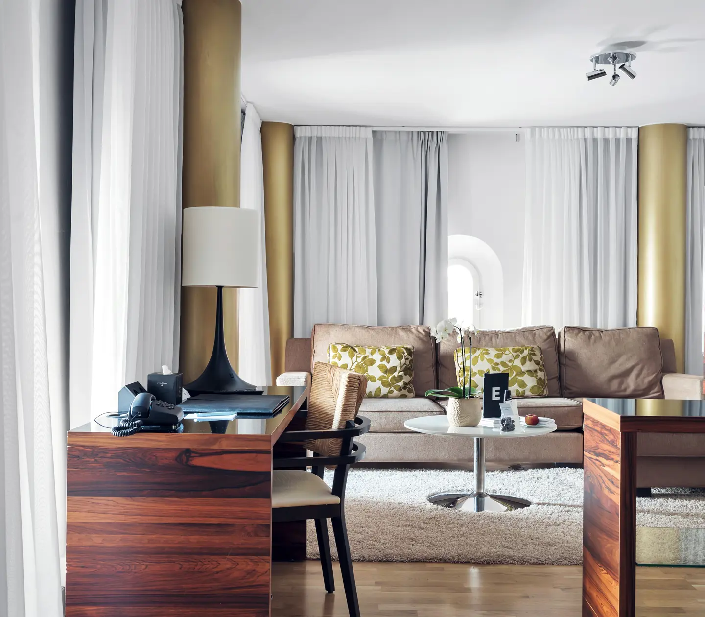 Bright suite with sofa group, desk and curtains along the walls