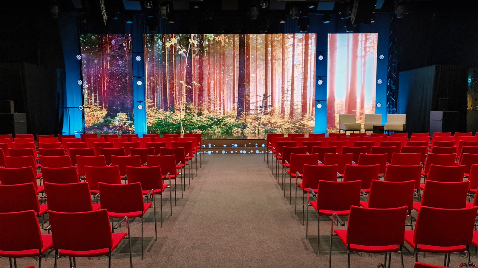 Konferenssal med biosittning, röda stolar, tv-studio, projektor