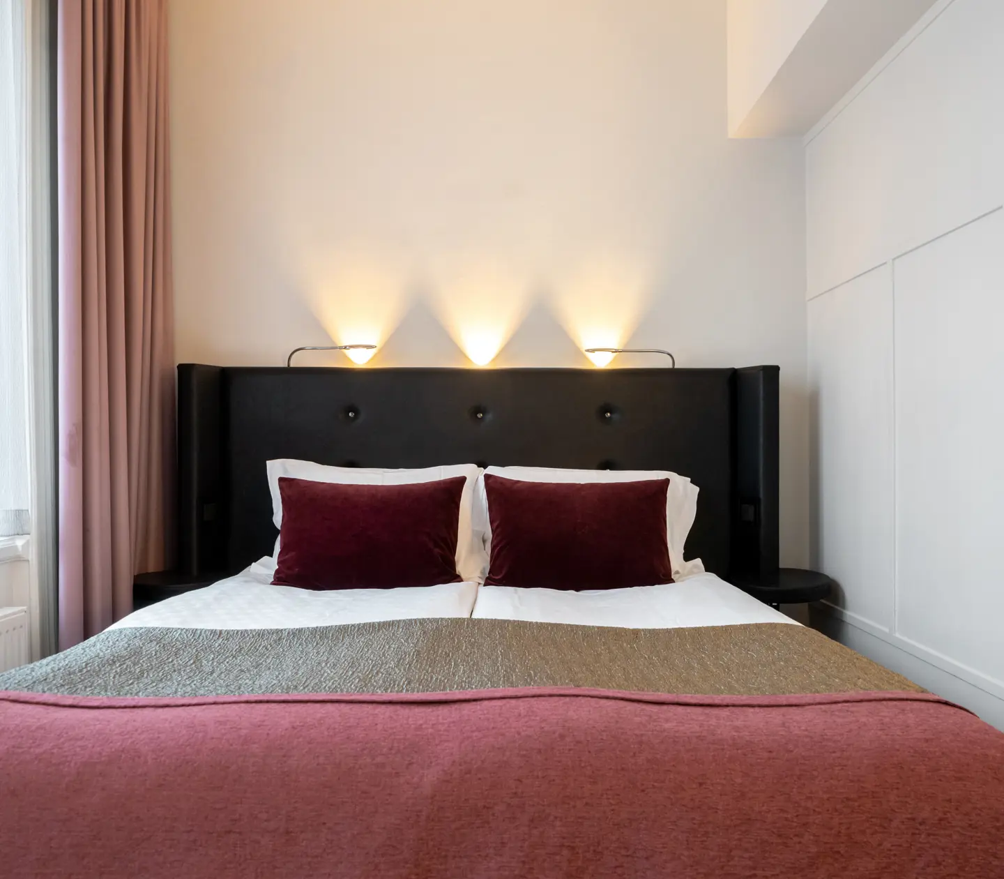 Hotel room with double bed with black headboard and pink bedspread