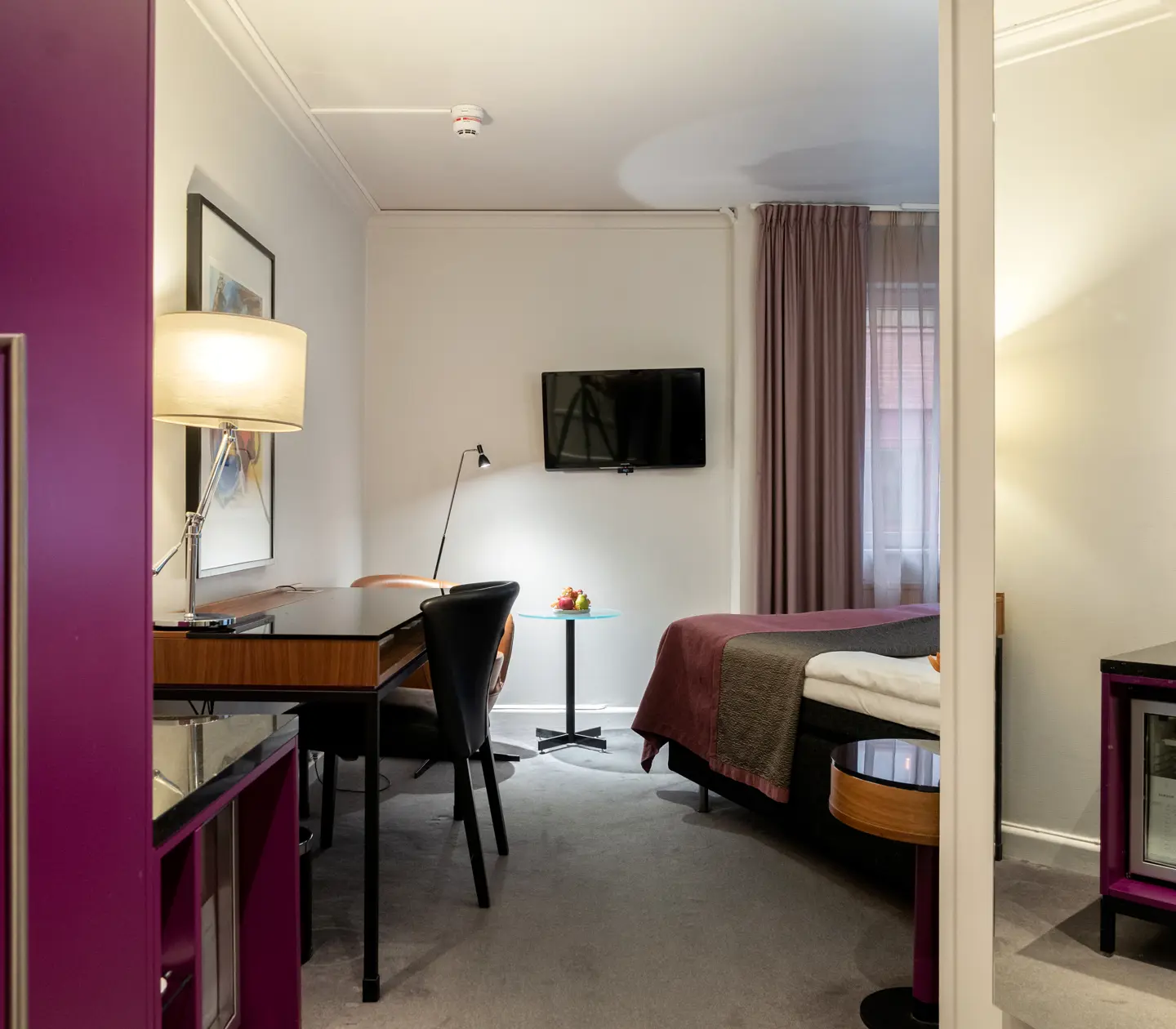 Hotel room with double bed, desk, blackboard, armchair, TV and window