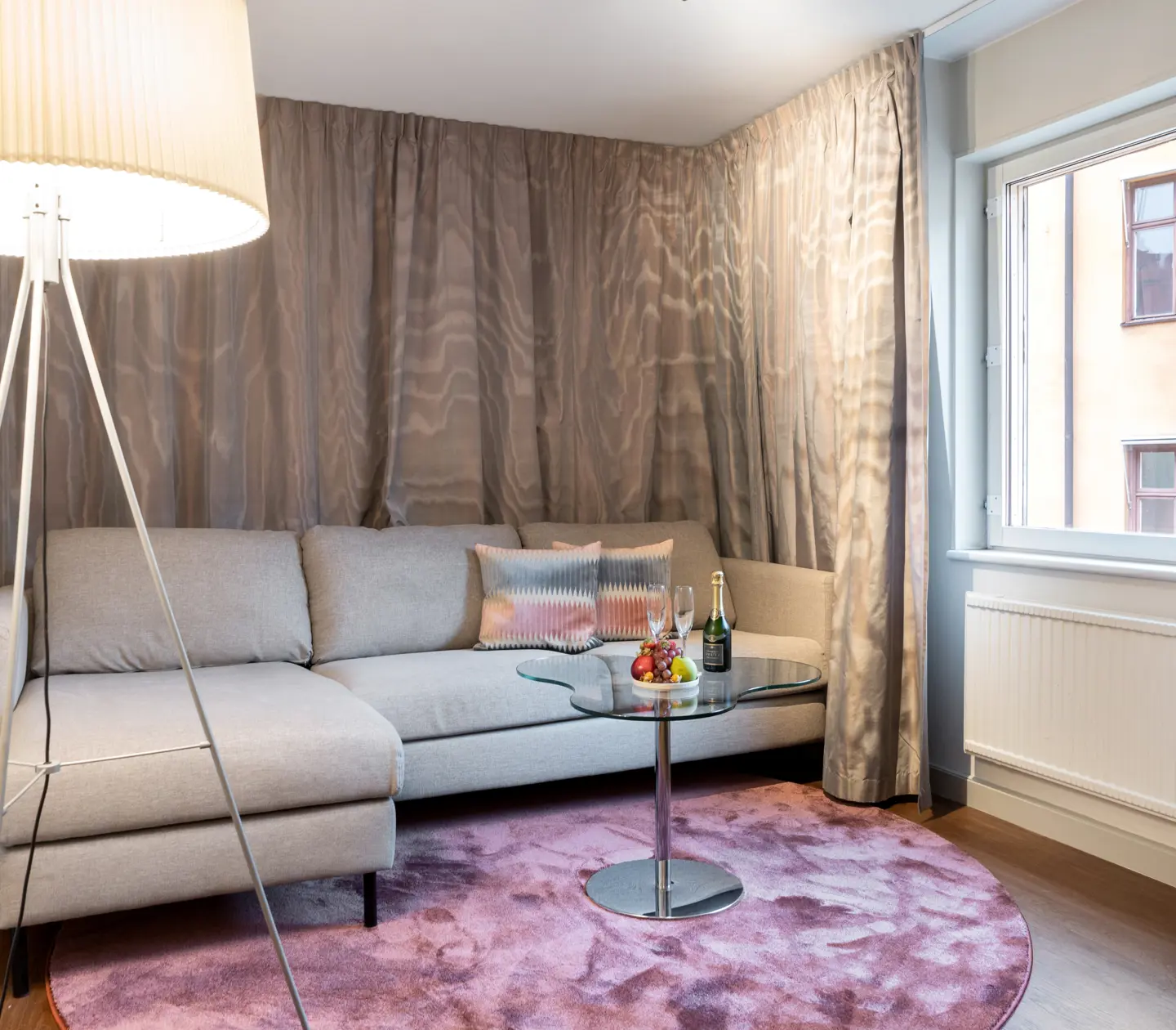 Comfortable hotel room with windows, curtains, sofa, carpet and table with fruit