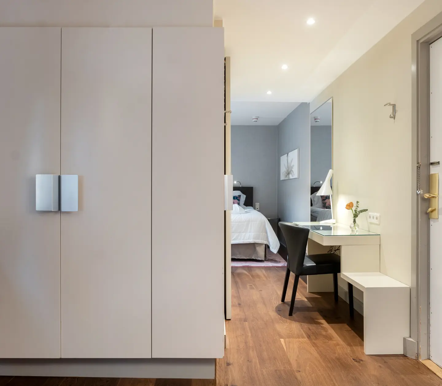 Bright hotel room with wardrobe, desk, mirror and double bed