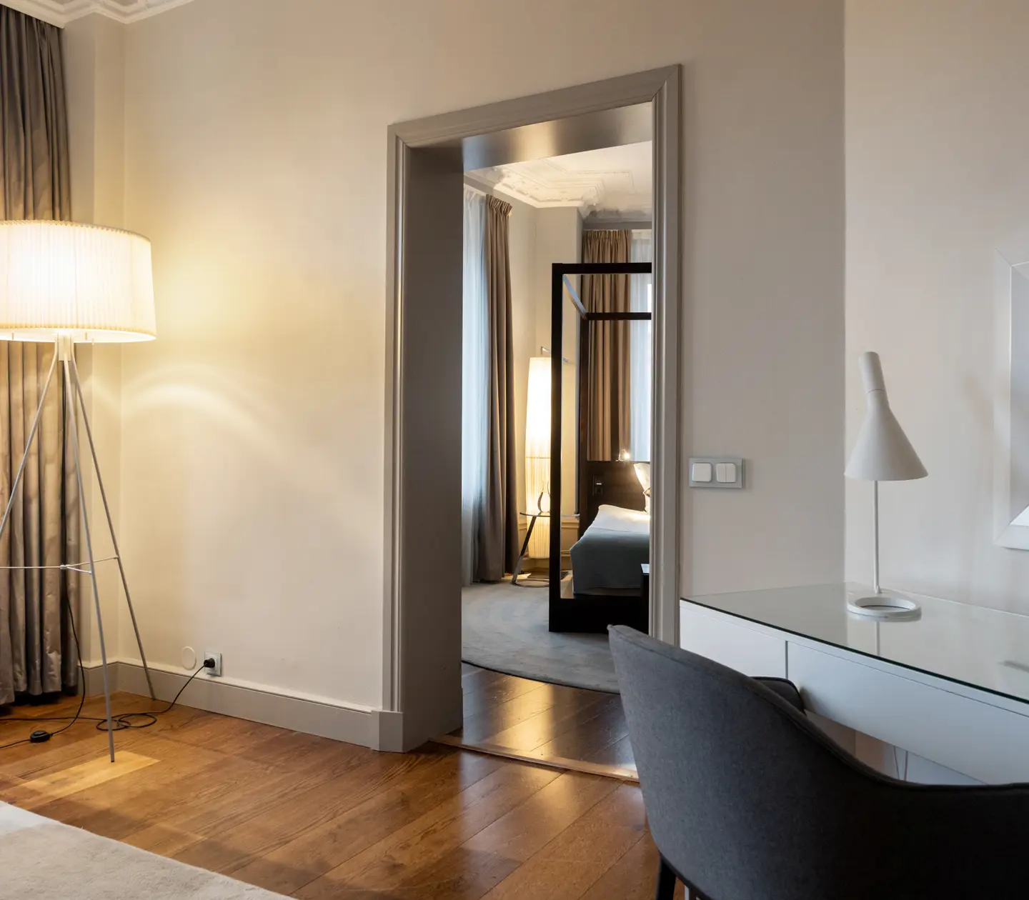 Bright hotel suite with desk, mirror, door to bedroom and floor lamp