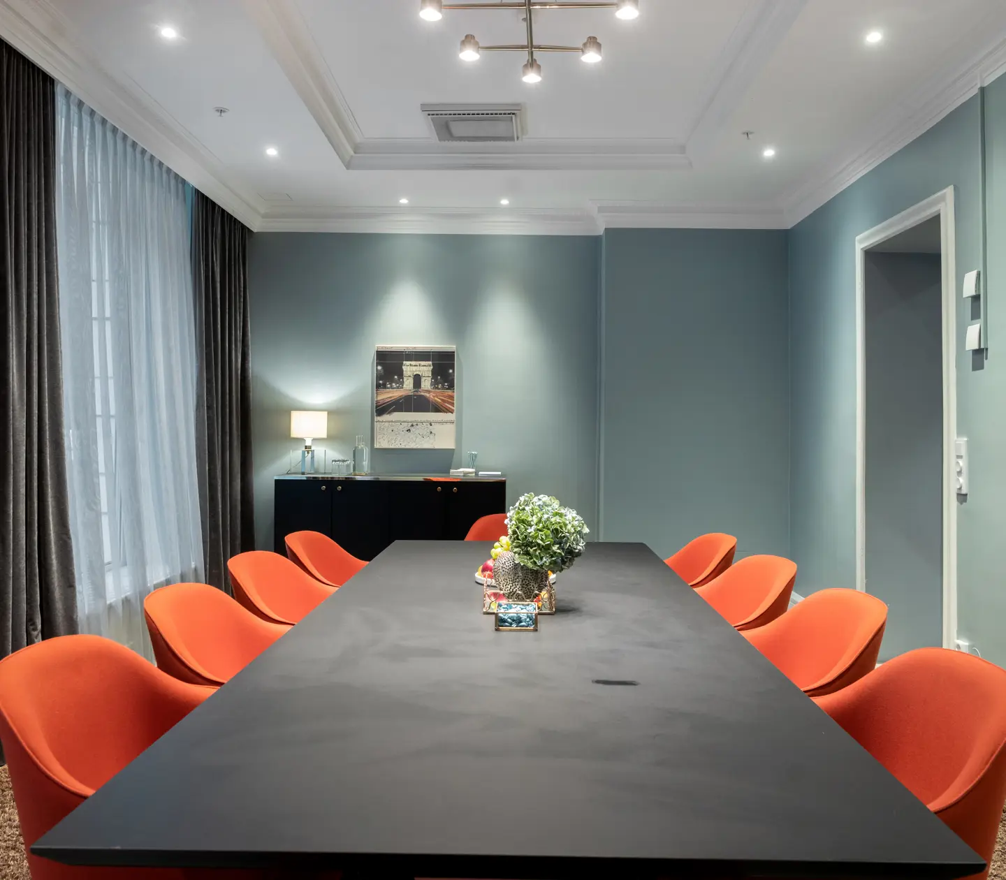 Light blue conference room with large gray conference table and red chairs around