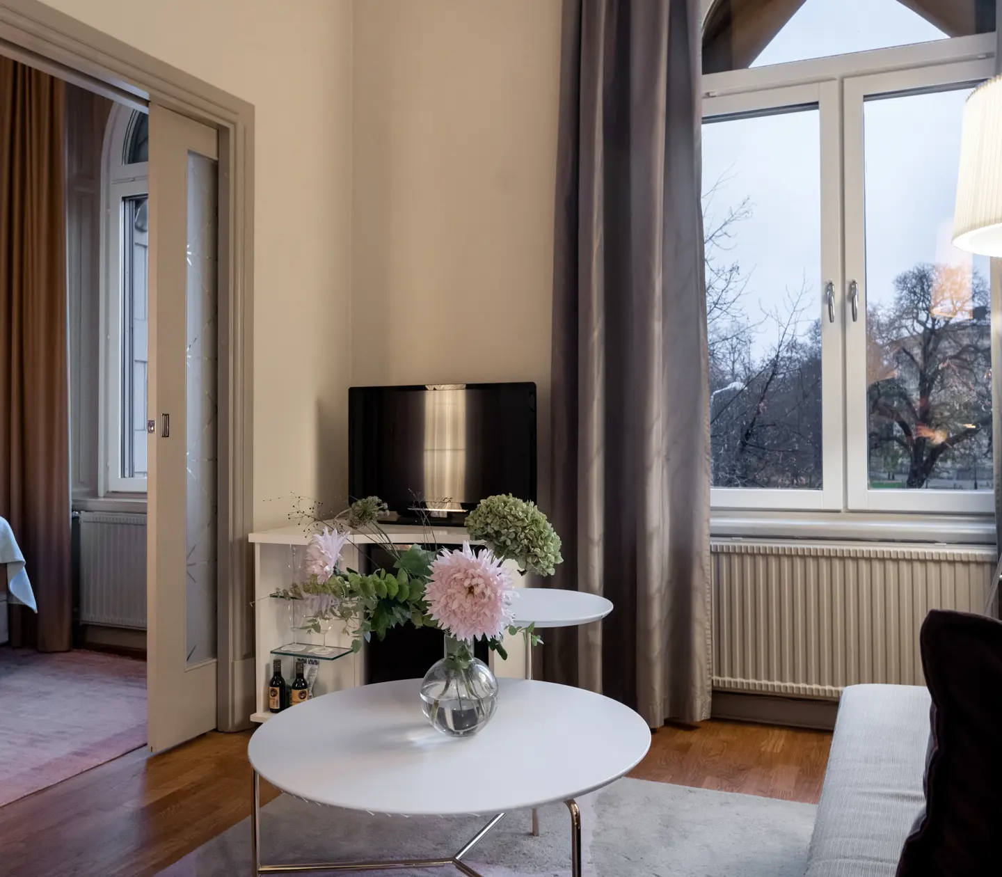Cozy hotel suite with door to bedroom, sofa, bouquet and large window