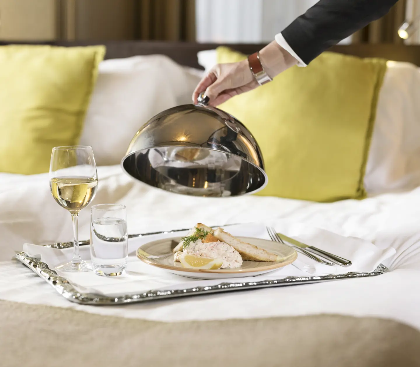 Room service served on the hotel bed in the form of Toast Skagen and a glass of white wine