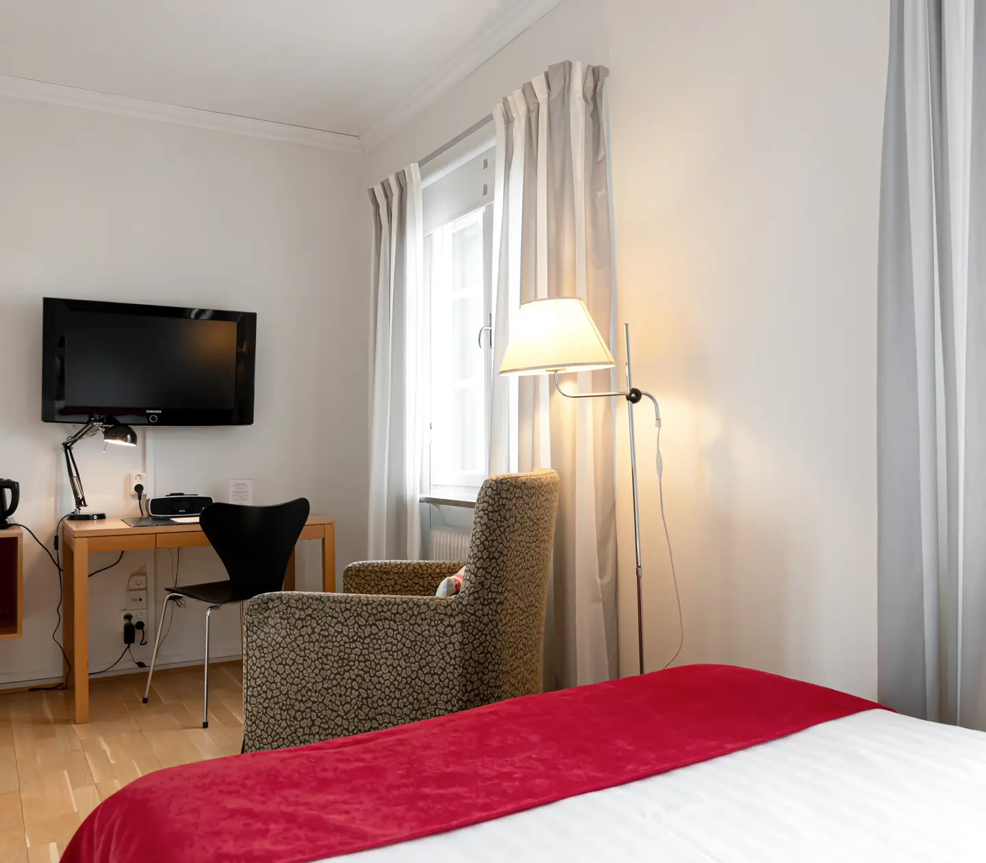 Bright hotel room with desk, armchair and TV