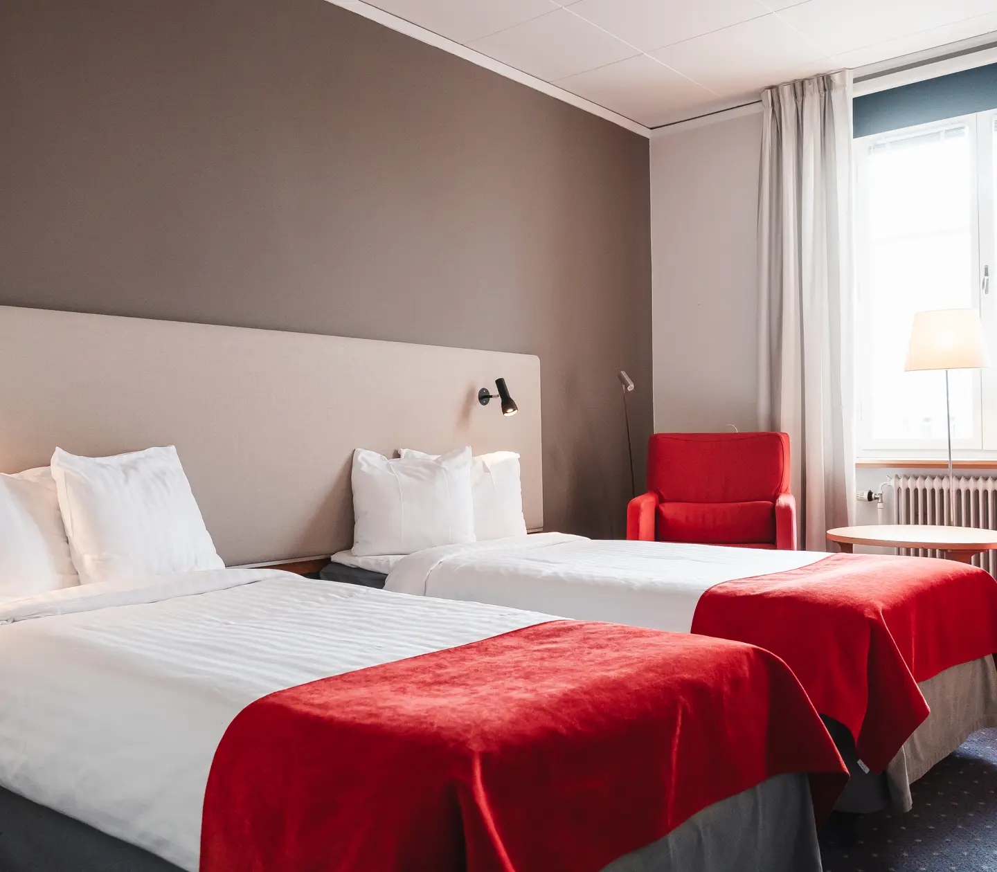 Cozy hotel room with beds, red armchairs and windows
