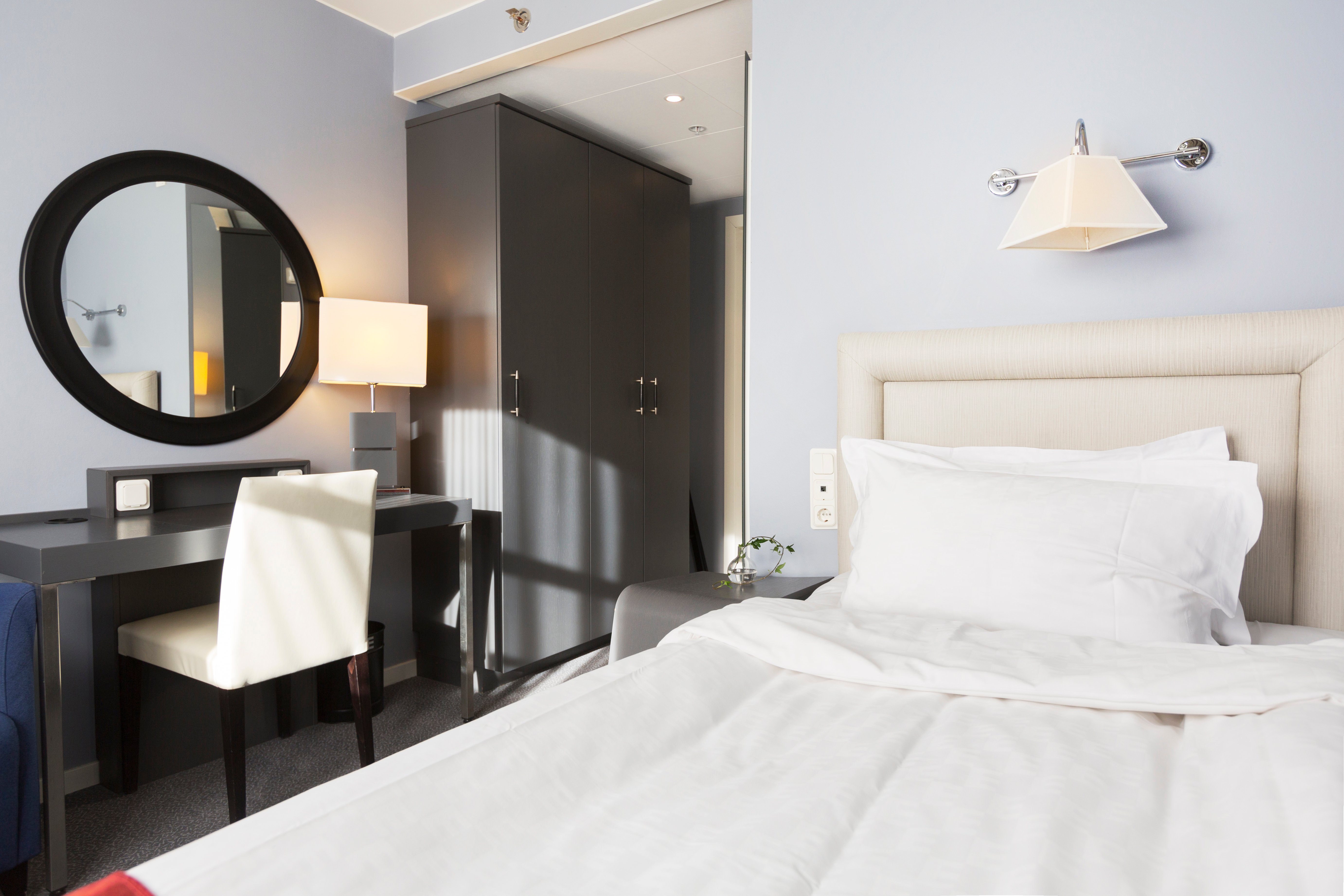 Litet hotellrum med säng, skrivbord och spegel