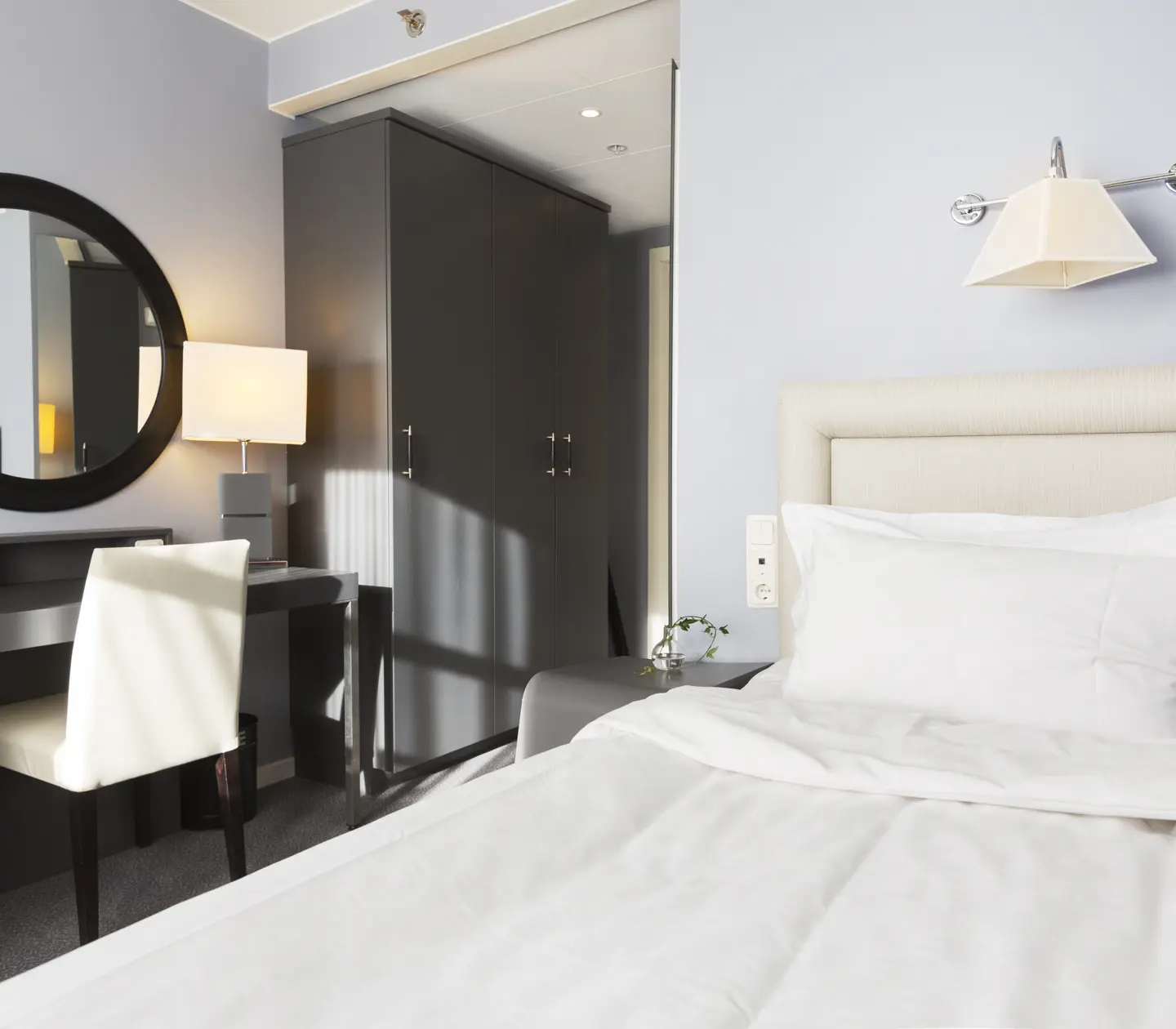 Small hotel room with bed, desk and mirror