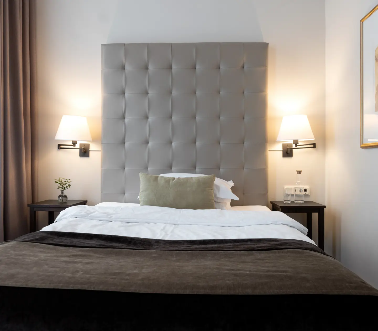 Small hotel room with bed, large gray headboard and bedside lamps