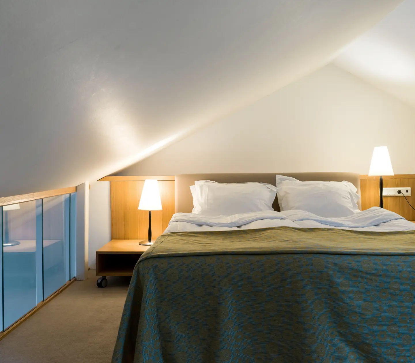 Bright hotel room with bed, glass railing and bedside lamps