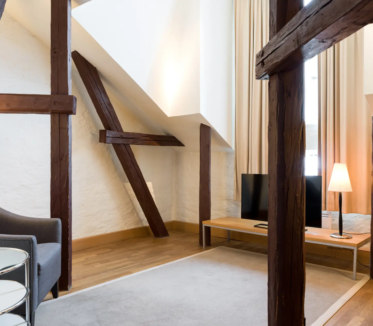 Bright hotel room with wooden beams from the ceiling, armchair and TV