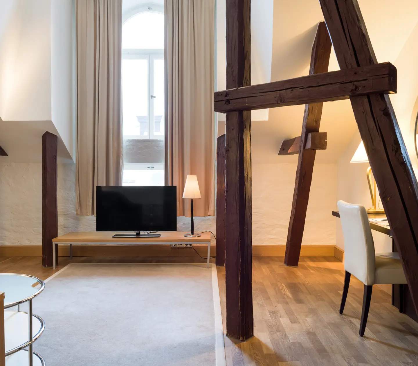 Bright hotel room with wooden beams from the ceiling, desk and TV
