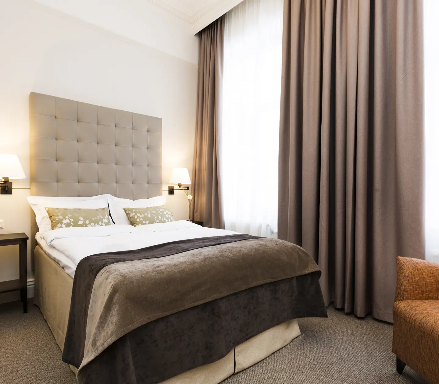 Bright hotel room with bed, gray headboard and armchair