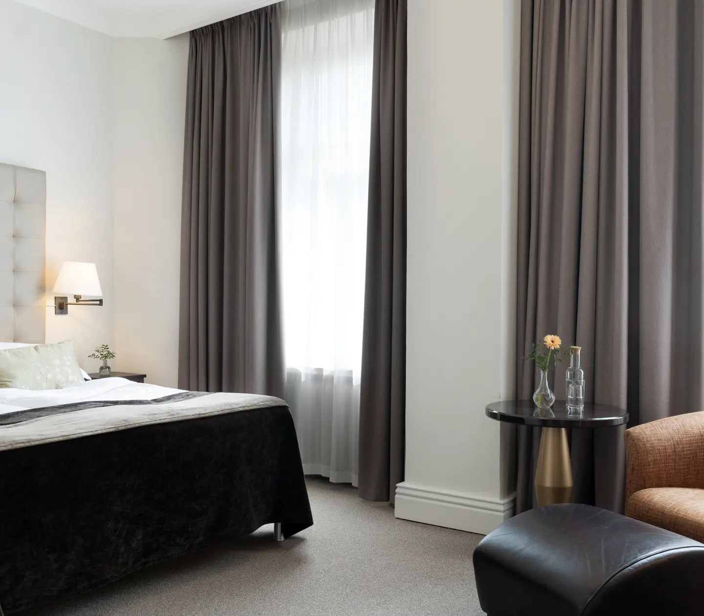 Bright hotel room with bed, white headboard and armchairs
