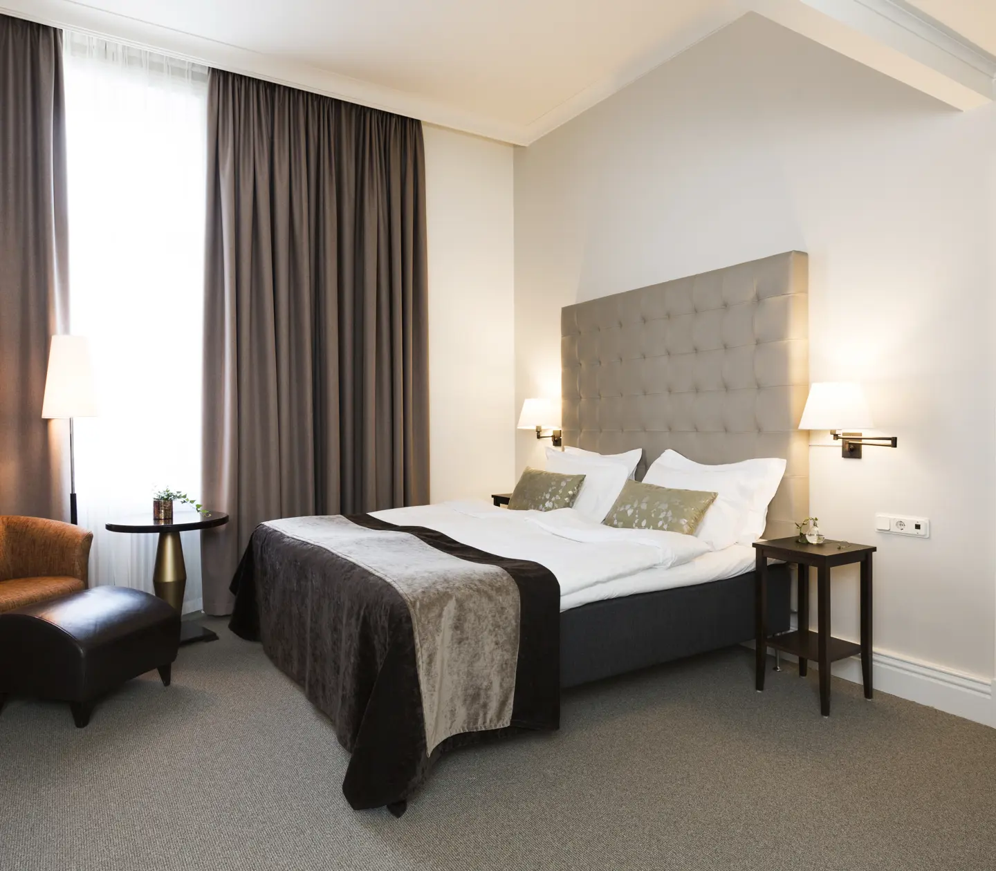 Bright hotel room with bed, gray headboard and armchairs
