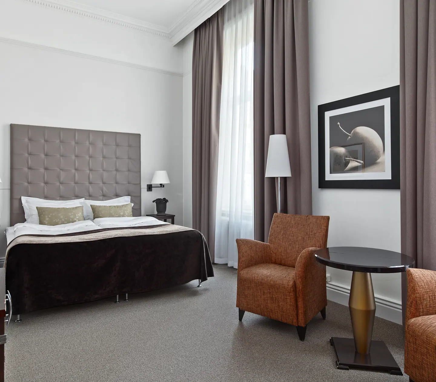 Bright hotel room with bed, gray headboard and armchairs