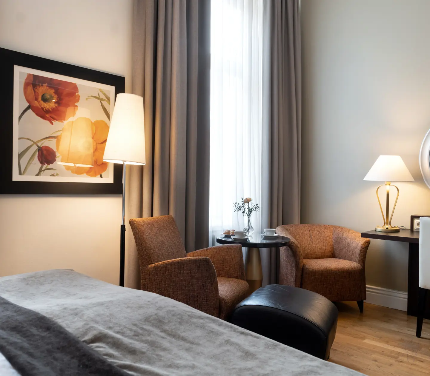 Bright hotel room with bed, desk and armchairs