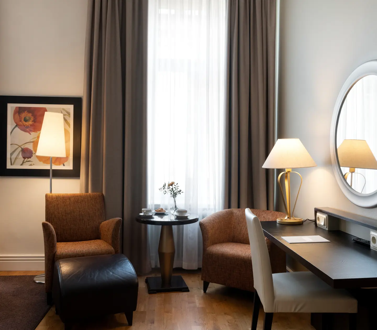Bright hotel room with large window, desk and armchairs