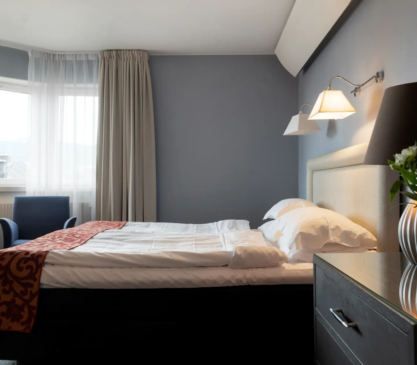 Bright hotel room with bed, white headboard and armchair
