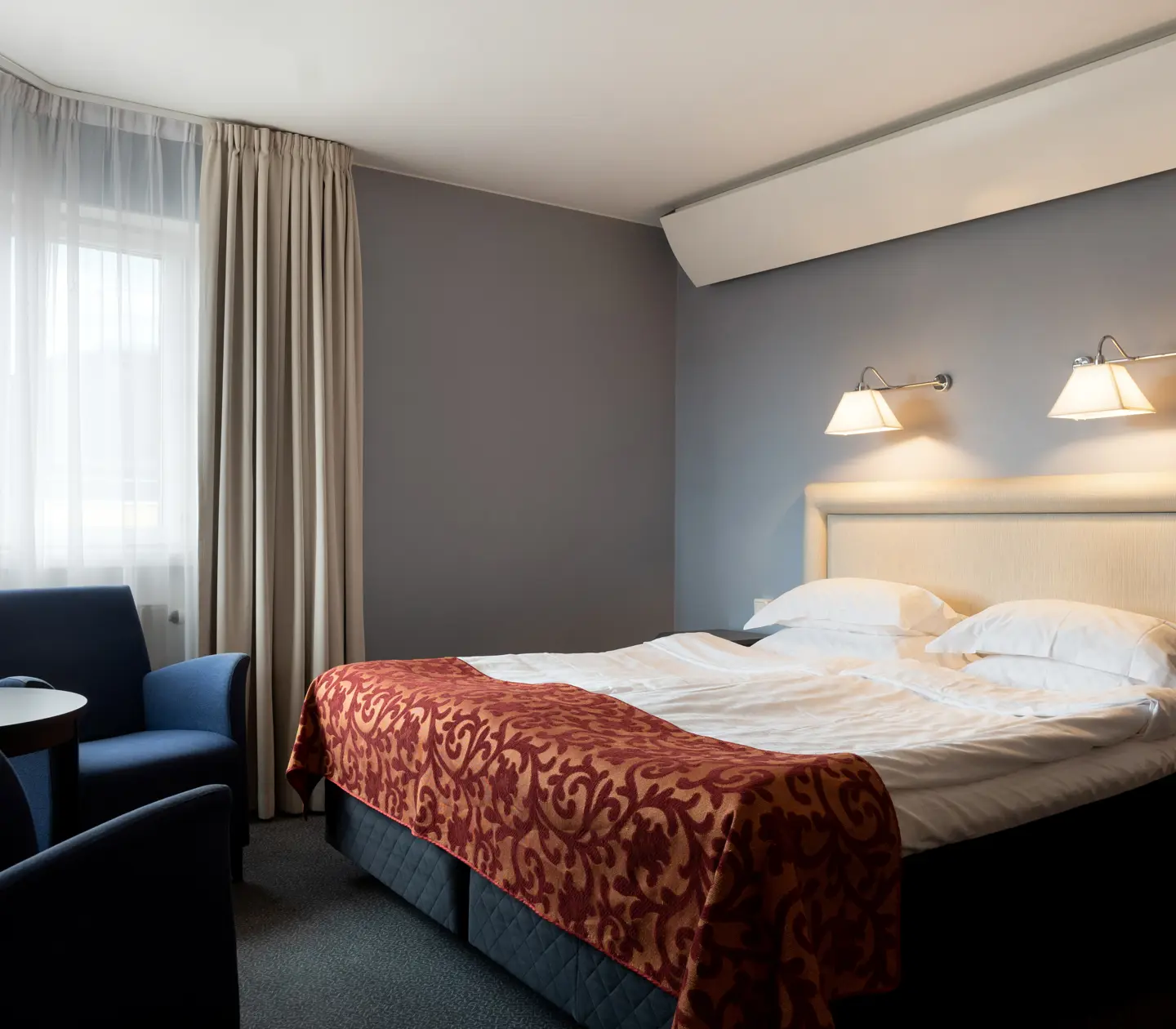 Bright hotel room with bed, white headboard and armchairs