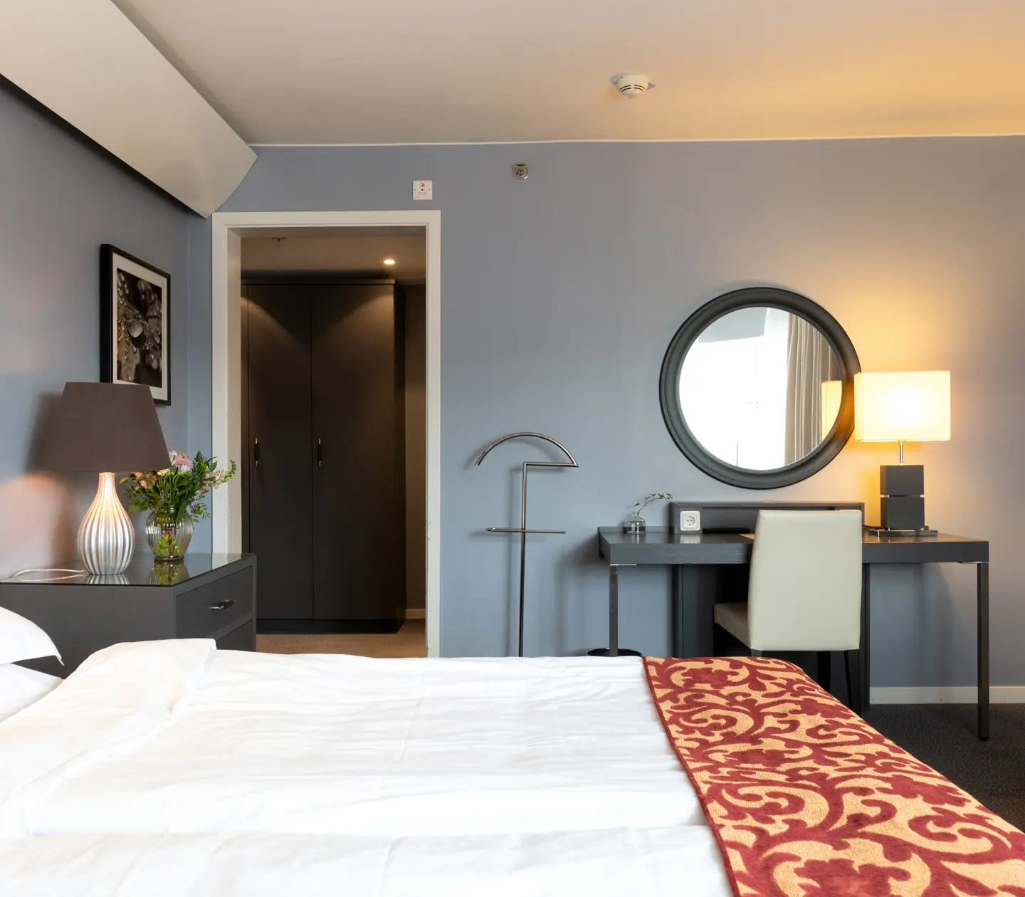 Bright hotel room with bed, desk and round mirror
