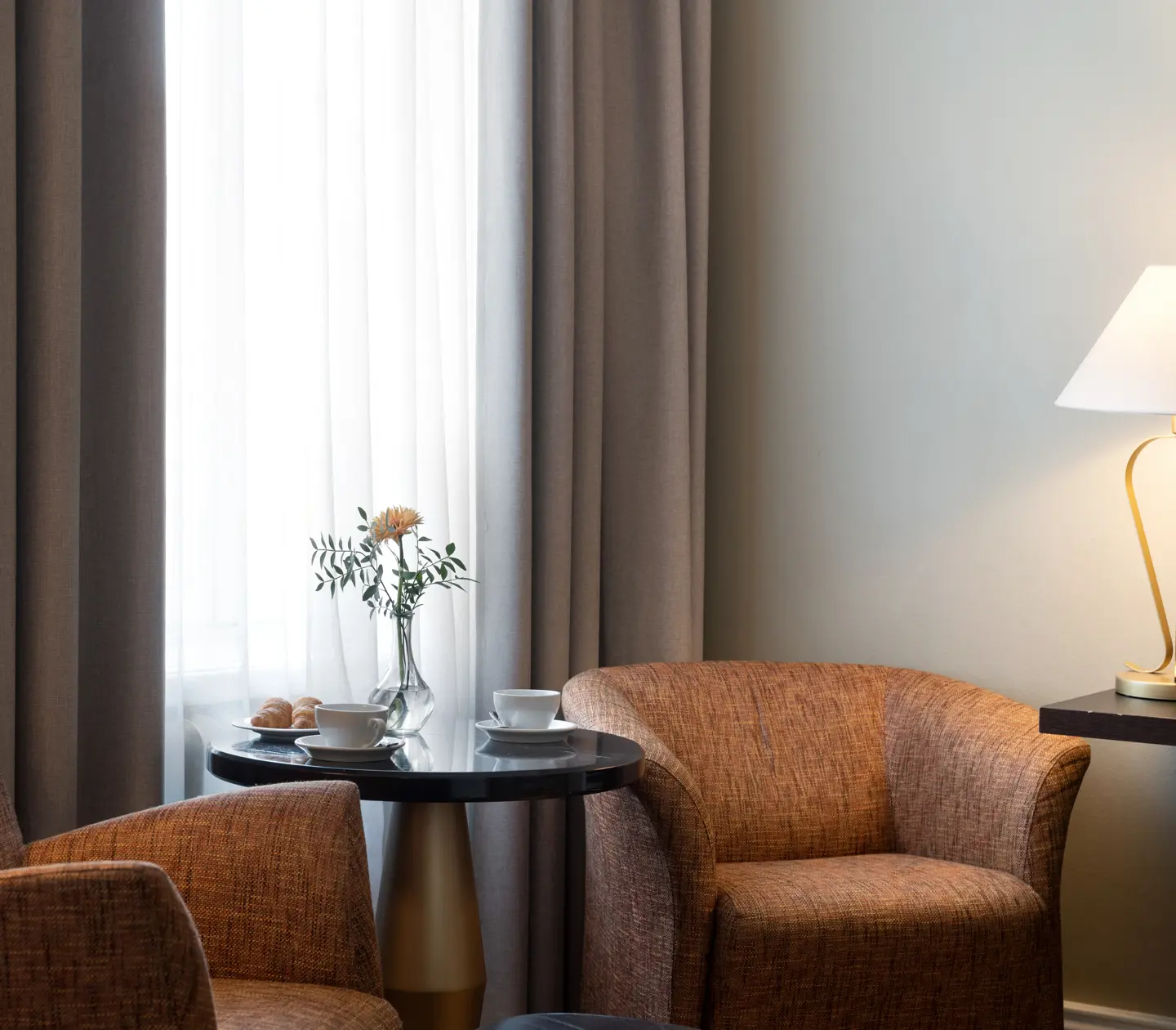 Bright hotel room with armchairs, table lamp and coffee cups on table