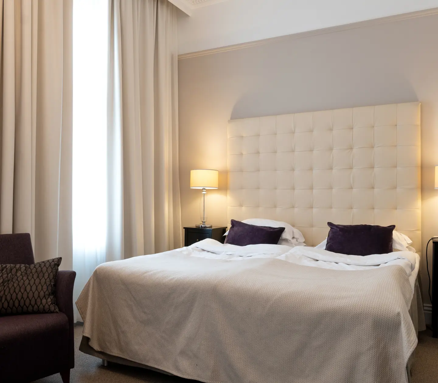 Bright hotel room with bed, white headboard and armchair