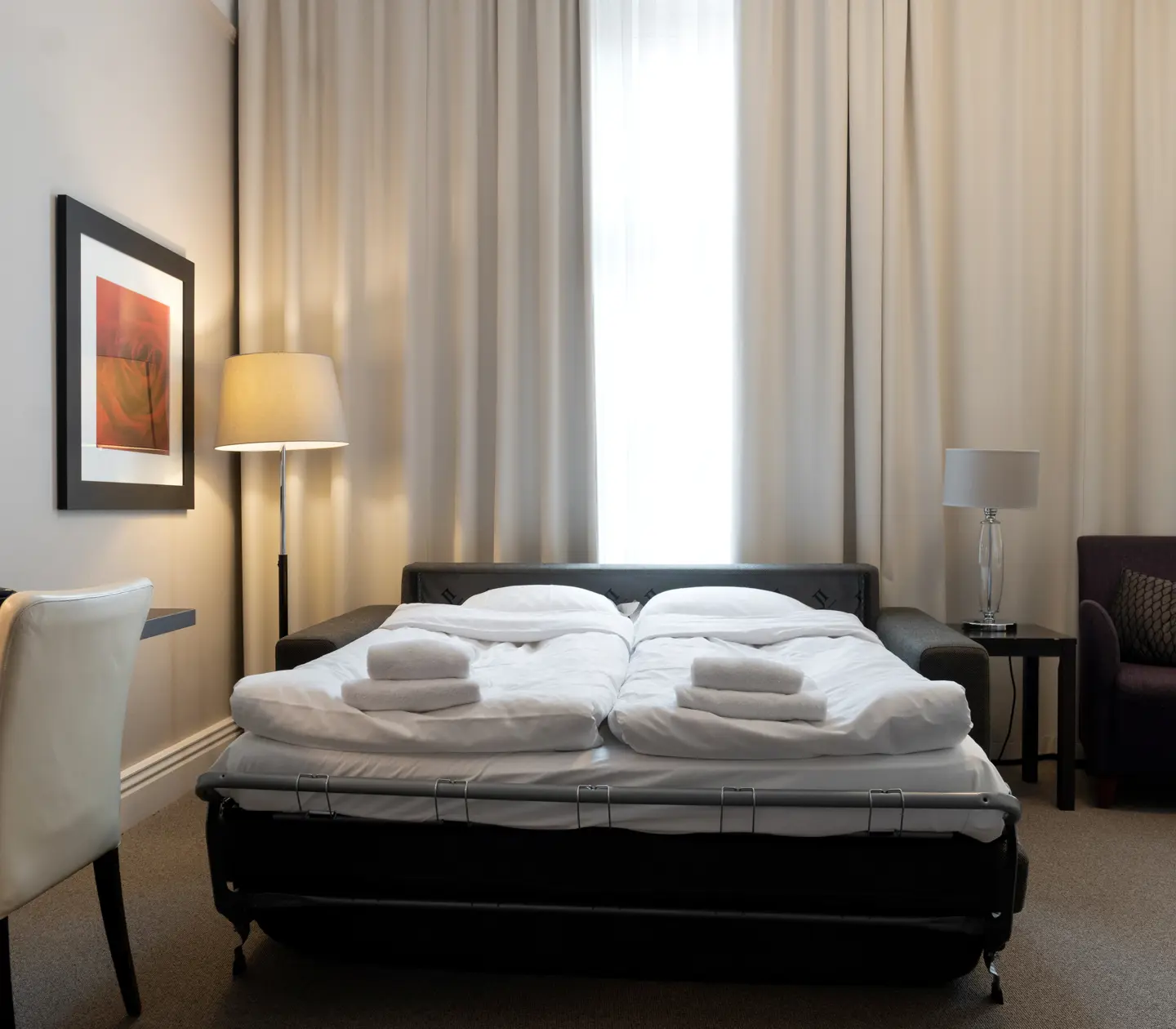 Bright hotel room with desk, armchair and sofa bed