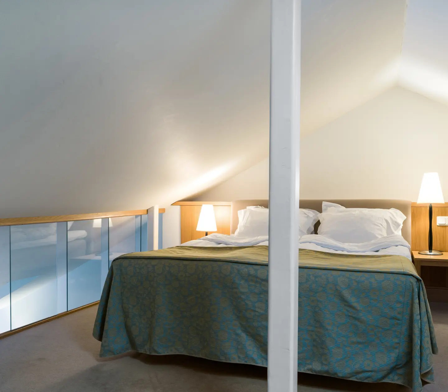 Bright suite with bed, bedside lamps and glass railing