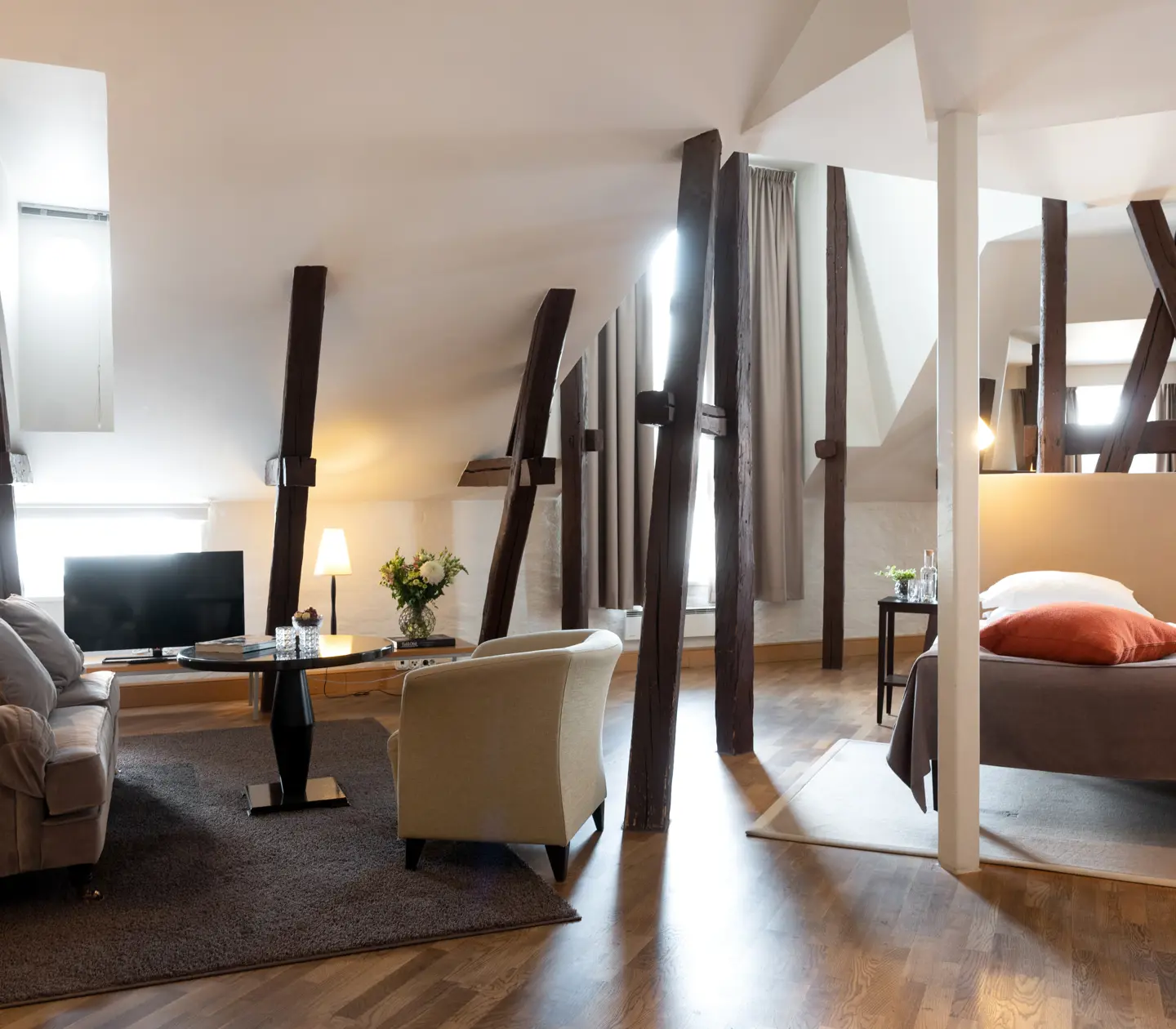 Hotel suite with bed, sofa group and wooden beams from the ceiling