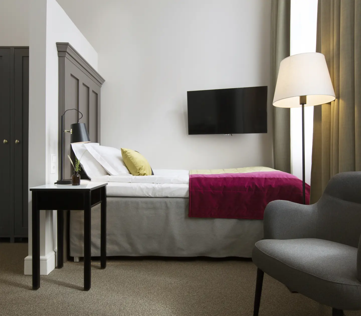 Bright hotel room with bed, wardrobe and armchair