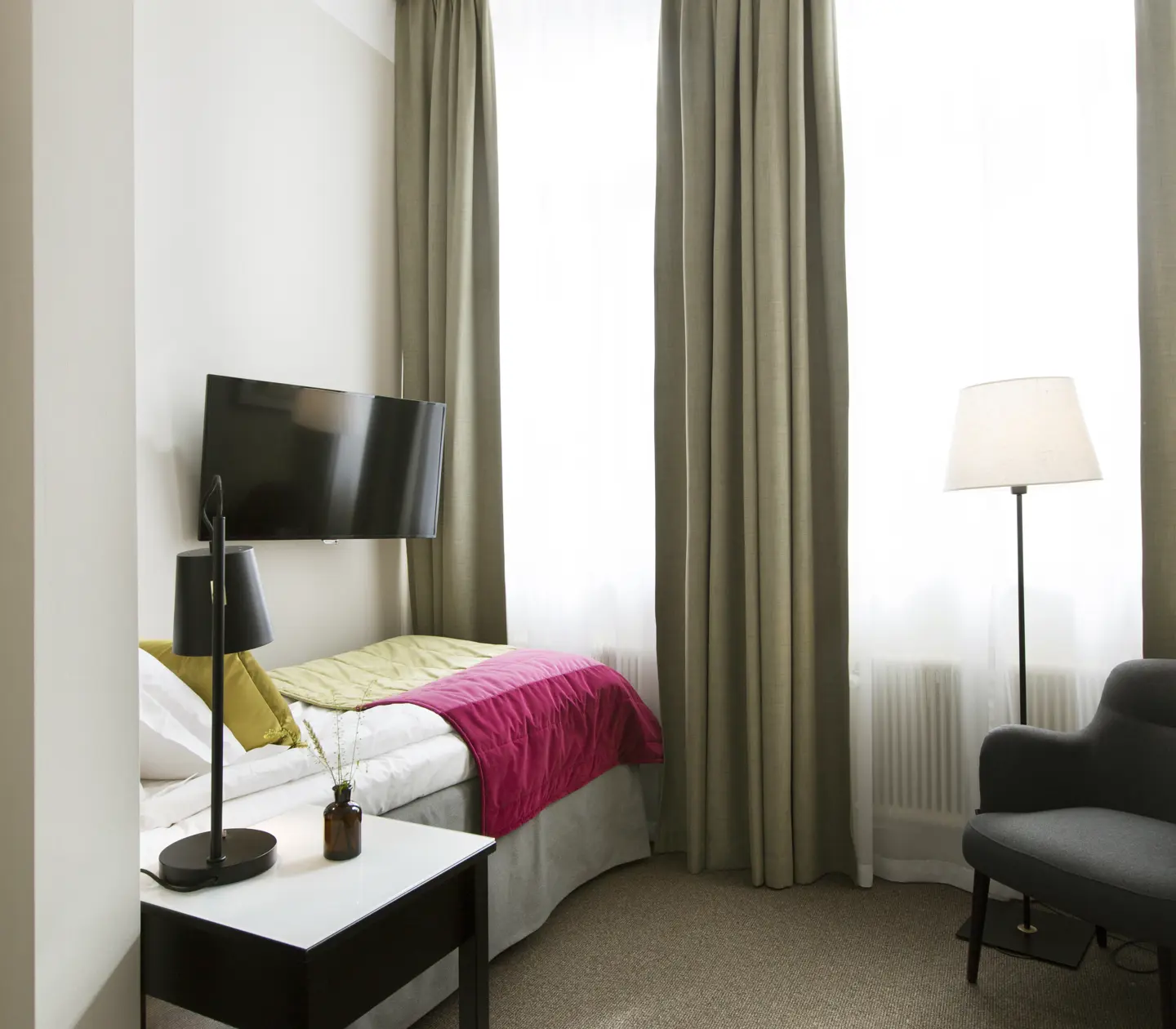Bright hotel room with bed, TV and armchair