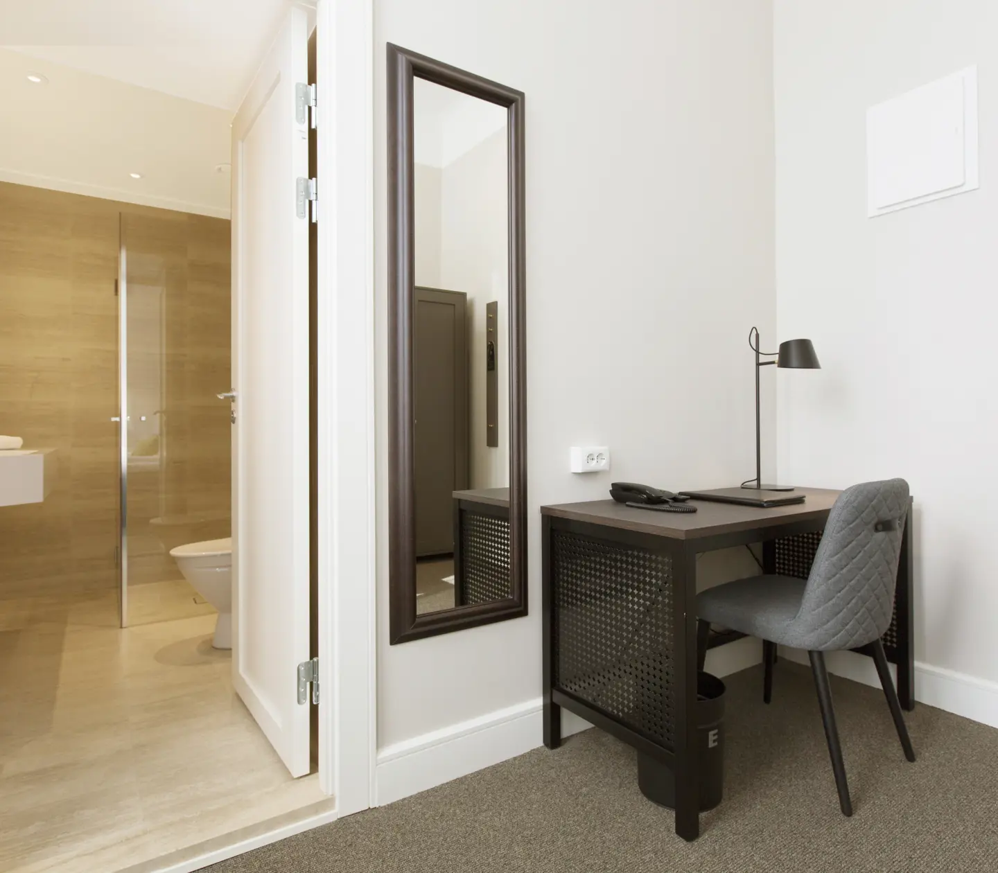 Bright hotel room with desk, mirror and bathroom door