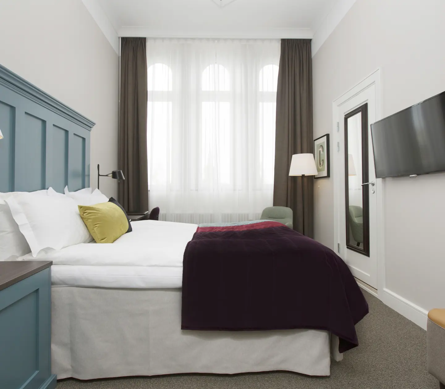 Bright hotel room with bed, large blue headboard and TV