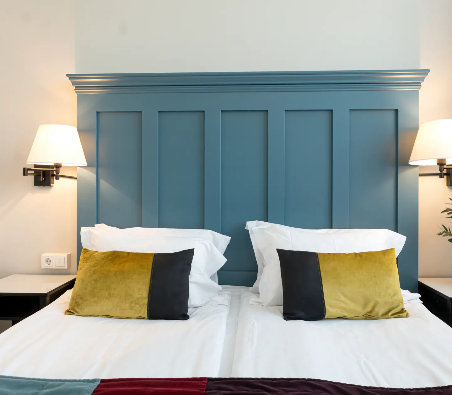 Bright hotel room with bed, large blue headboard and bedside lamps