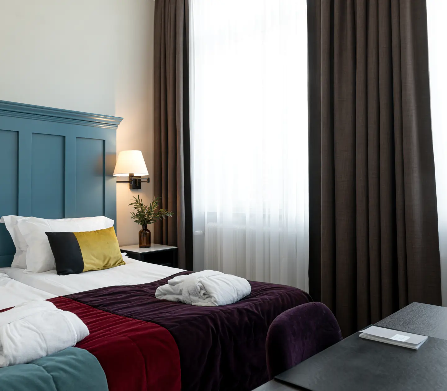 Bright hotel room with bed, large blue headboard and bathrobes