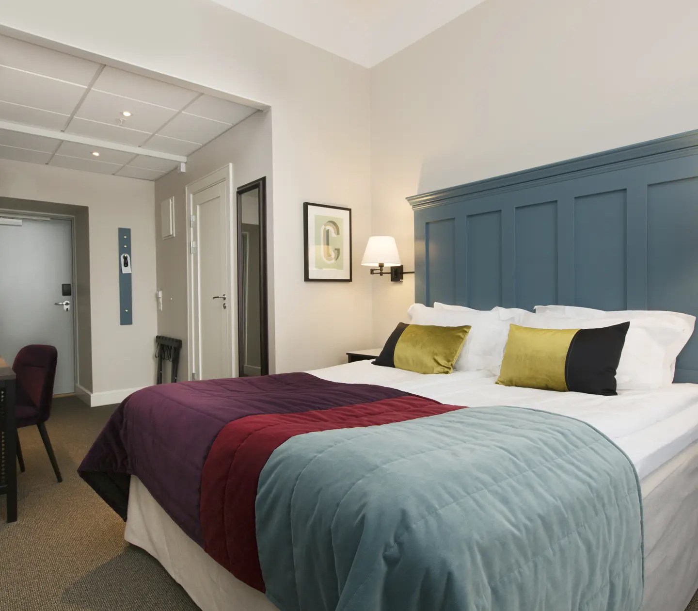 Bright hotel room with bed, large blue headboard and desk