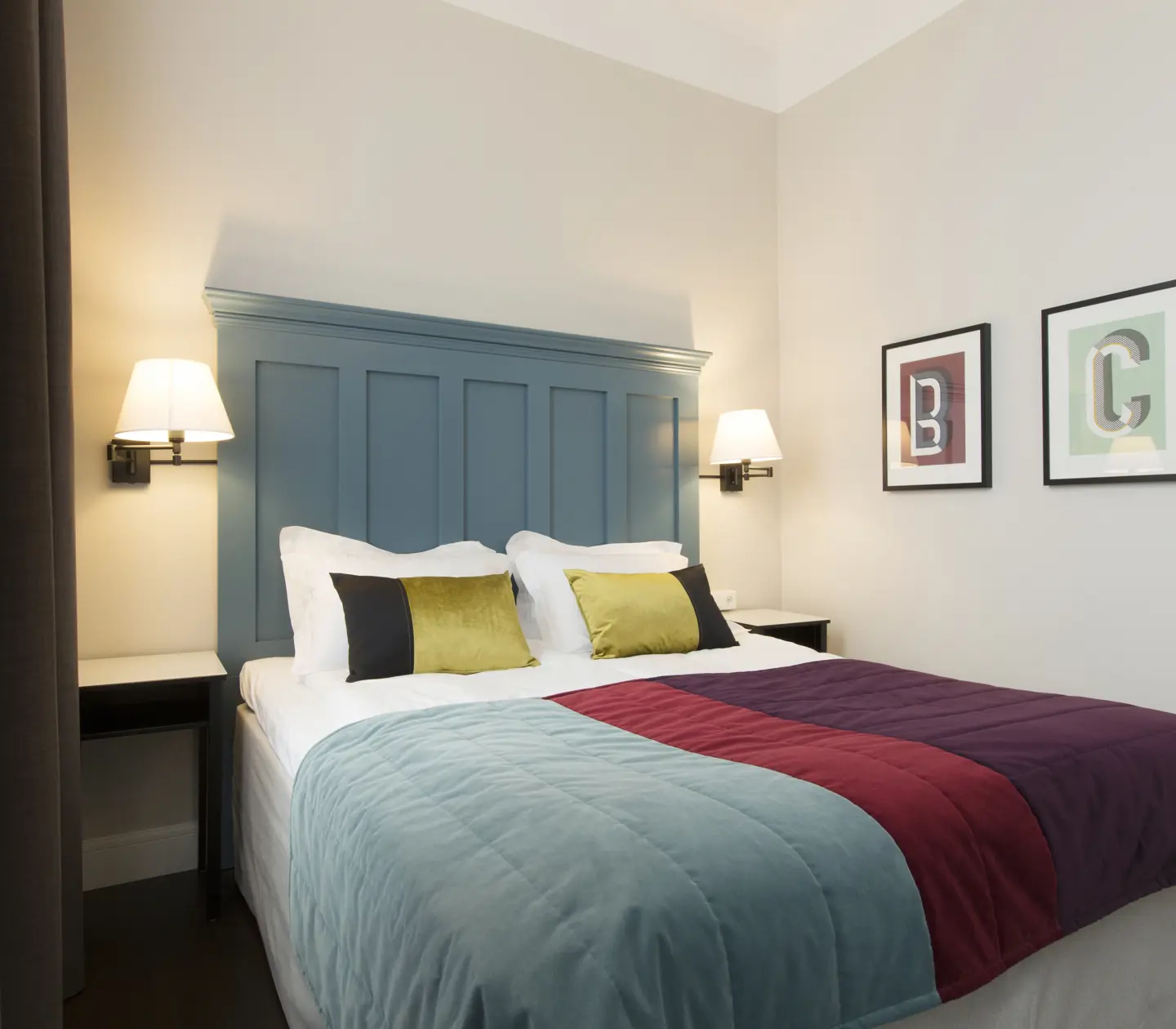 Bright hotel room with bed, large blue headboard and bedside tables