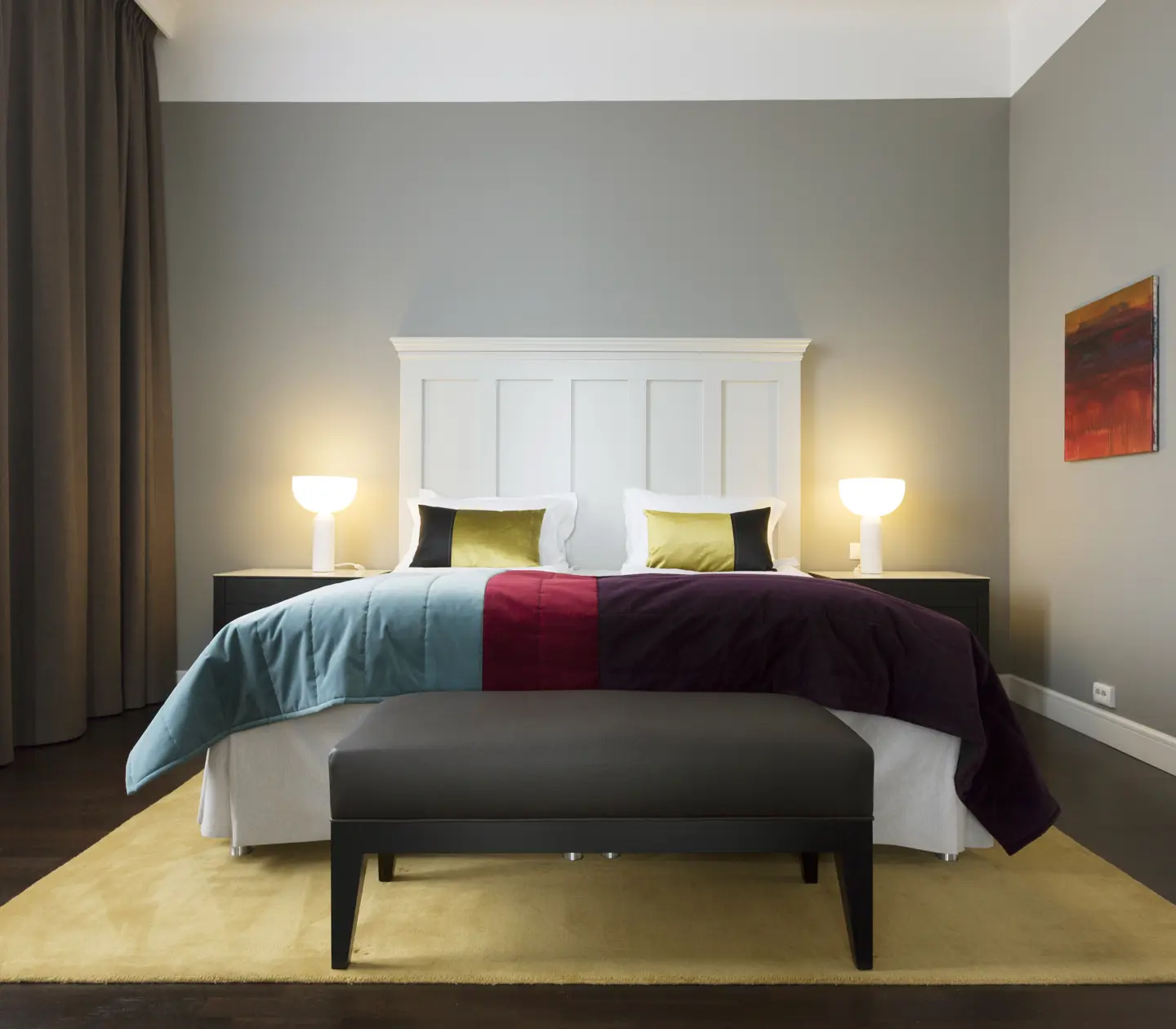 Bright suite with bed, large white headboard and bedside lamps